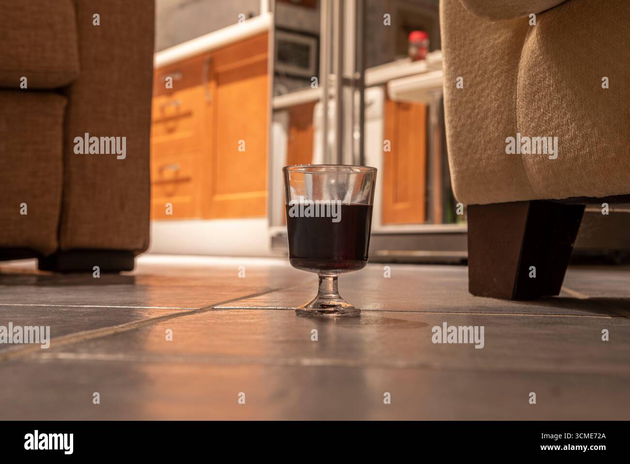 Un piccolo bicchiere di vino rosso su un pavimento piastrellato in un appartamento Foto Stock