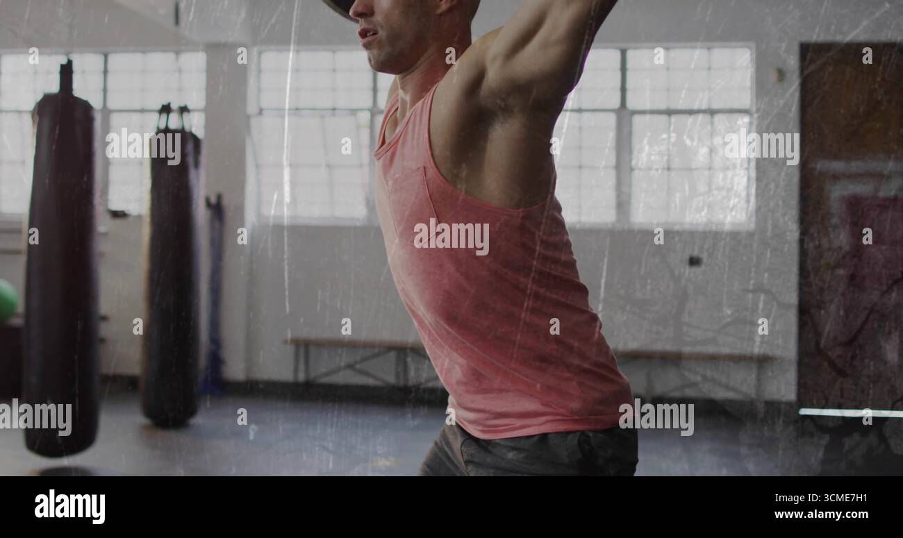 Esecuzione di una pressa a soffitto uomo muscoloso all'interno della palestra, con sacchi di punzonatura appesi e palla da ginnastica Foto Stock
