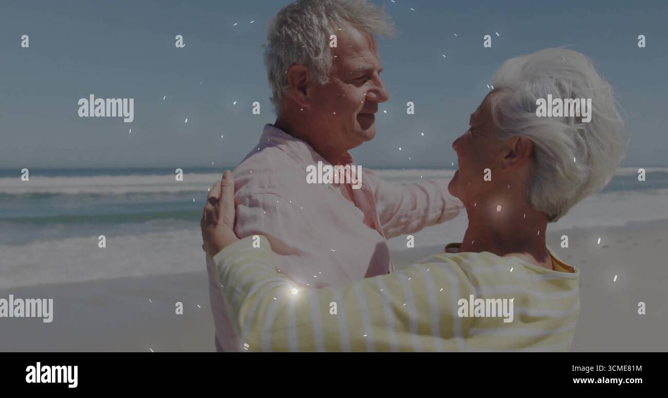 Abbracciare una coppia senior in piedi sulla spiaggia di sabbia, sorridere con camicia rosa pastello e top a righe Foto Stock