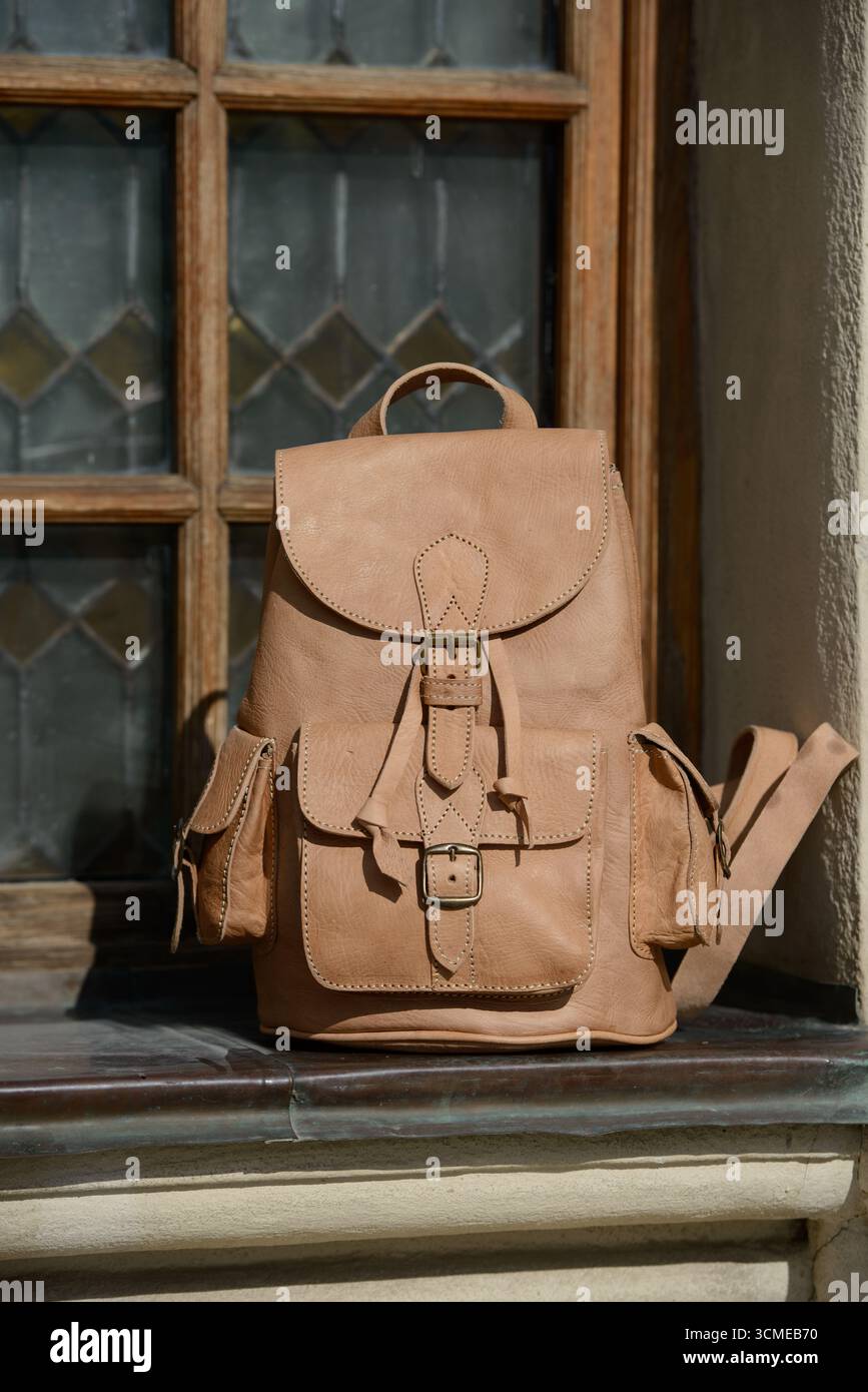 Uno zaino in pelle beige di alta qualità con fibbie e tasche dettagliate è presentato su un davanzale rustico, evidenziando il suo design elegante e vintage. Foto Stock