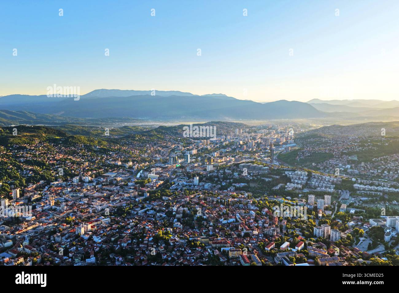 Ampia immagine panoramica con drone della valle di Sarajevo con edifici cittadini, colline e montagne sotto la luce del giorno estivo Foto Stock