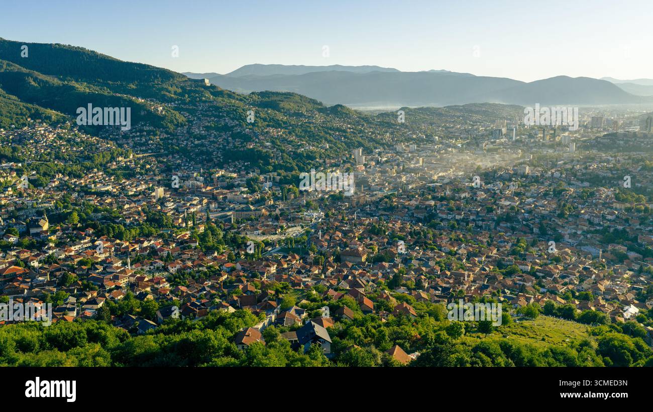 DefaultVai alla vista panoramica della città di Sarajevo con case residenziali, colline e luci mattutine che illuminano la valle Foto Stock