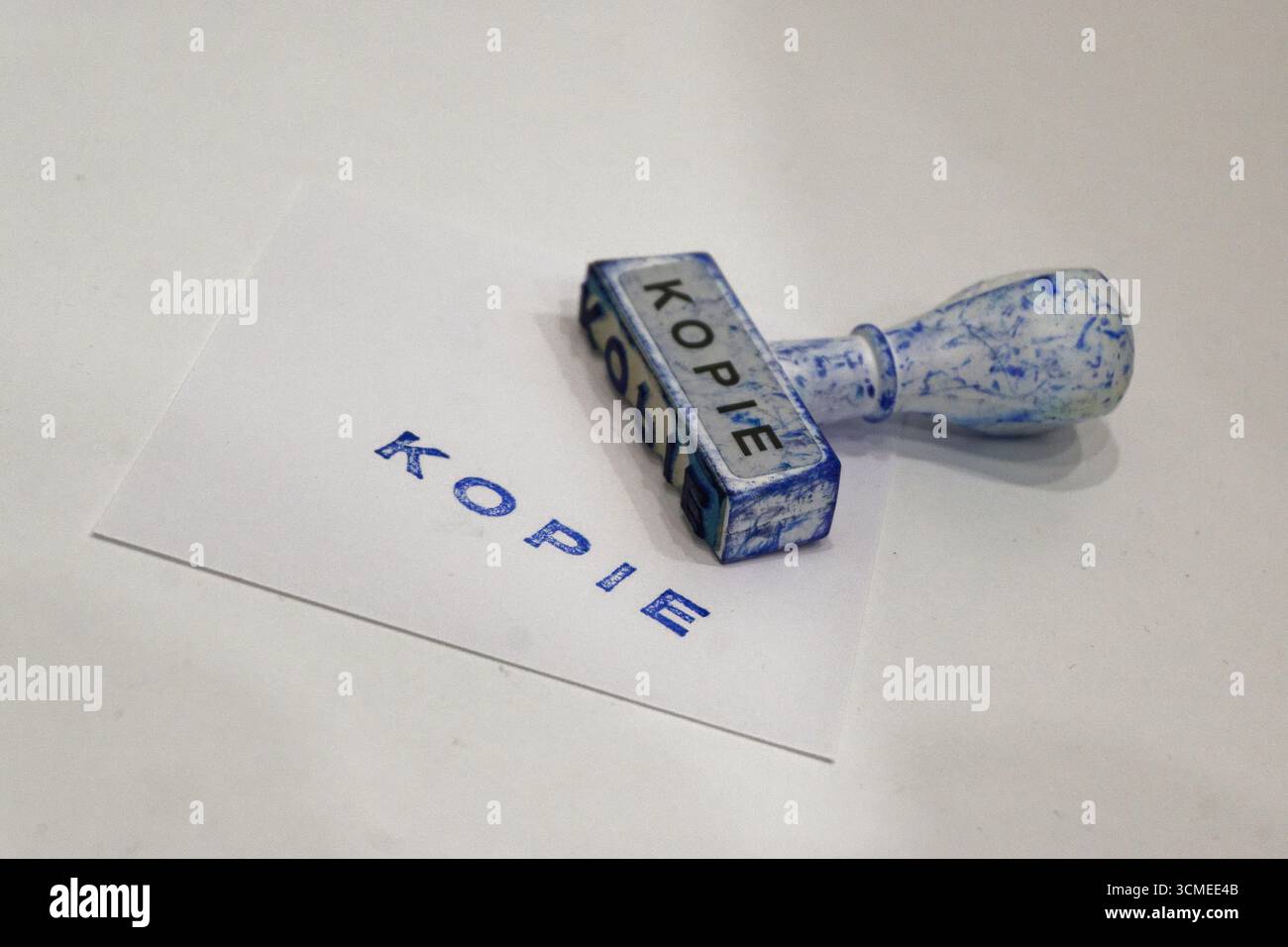 Un unico francobollo kontor buero dell'ufficio poggia accanto a un foglio bianco contrassegnato con una copia in inchiostro blu, l'impronta nitida è centrata. Sfondo pulito e impostazione semplice Foto Stock