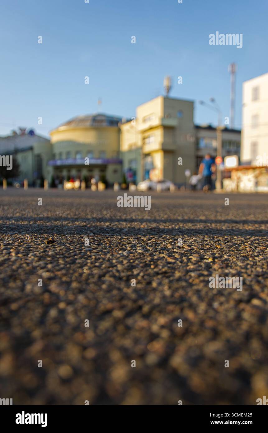 Vista ad angolo basso della superficie stradale asfaltata con edifici urbani sfocati alle spalle. Foto Stock