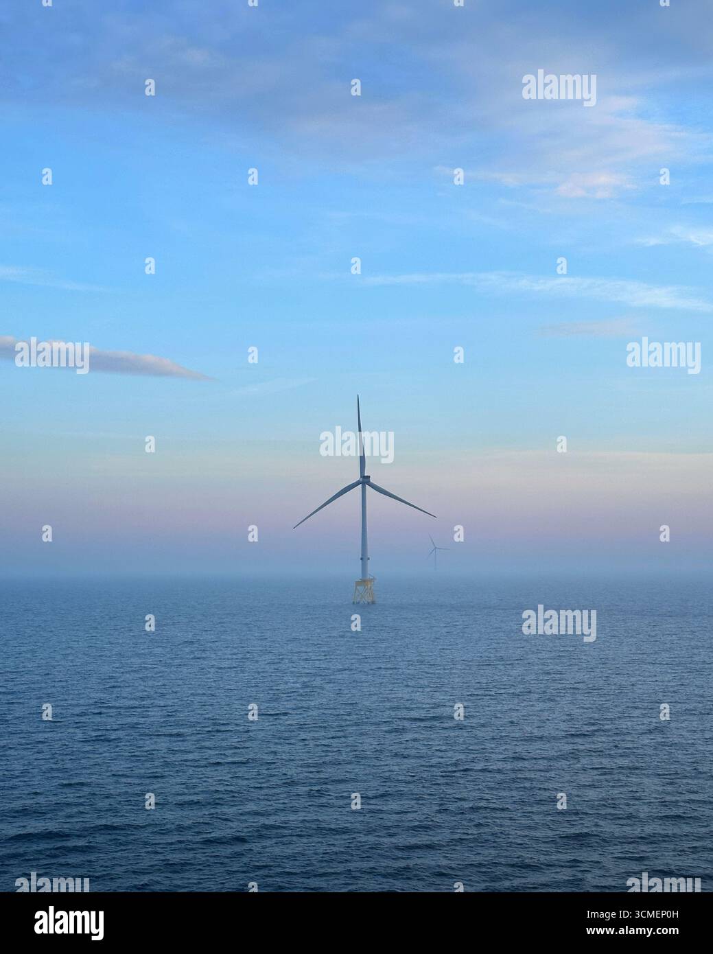 Turbine eoliche offshore nel Mare del Nord con nebbia mattutina e cielo pastello, infrastrutture di energia rinnovabile in un ambiente oceanico calmo. Foto Stock