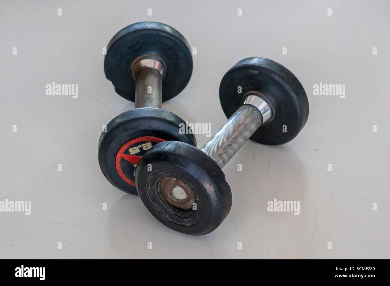 Due vecchi manubri da 2,5 kg si trovano fianco a fianco su un pavimento di palestra, le loro superfici usurate raccontano una storia di dedizione alla salute, al sollevamento pesi e all'esercizio fisico. Foto Stock
