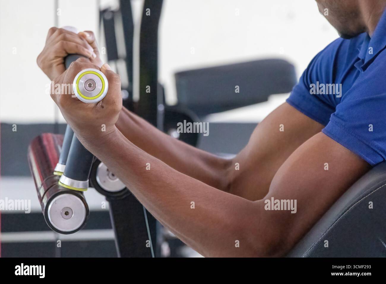 Primo piano della mano di un uomo afferrando una maniglia e sollevando una macchina per arricciatura bicipite caricata a lastra, mostrando la costruzione muscolare e l'allenamento di forza Foto Stock