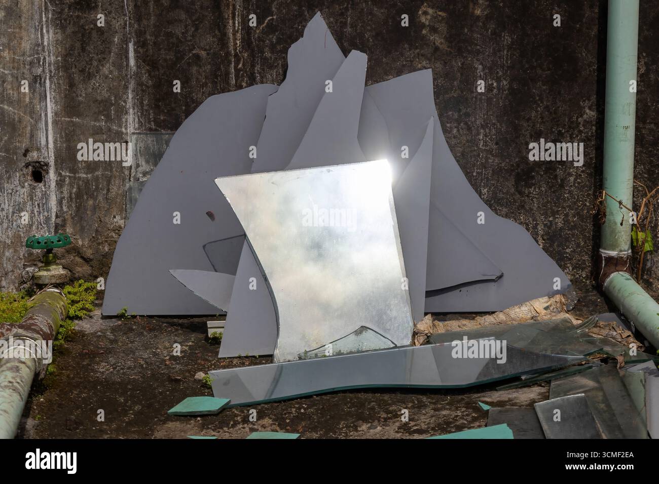 Frammenti di specchi rotti e rotti si trovano sparsi su un vecchio tetto di cemento sporco, creando un accattivante schema astratto di distruzione e riflessi Foto Stock