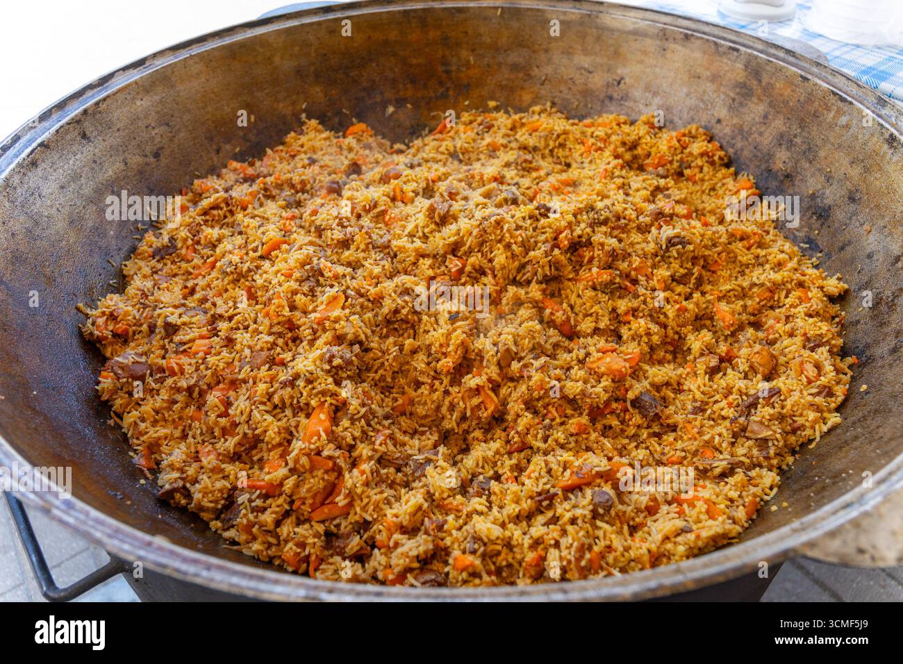 Un grande calderone metallico con stufati di pilaf uzbeki preparati al momento in un vivace festival di Street food, che mostra cucina tradizionale. Foto Stock