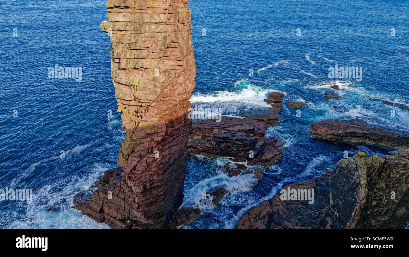 Old Man of Stoer nel Sutherland, Scozia, 200 piedi o 60 metri di arenaria di pietra arenaria di Torridonian, con sole mattutino, surf selvaggio e scalatori Foto Stock