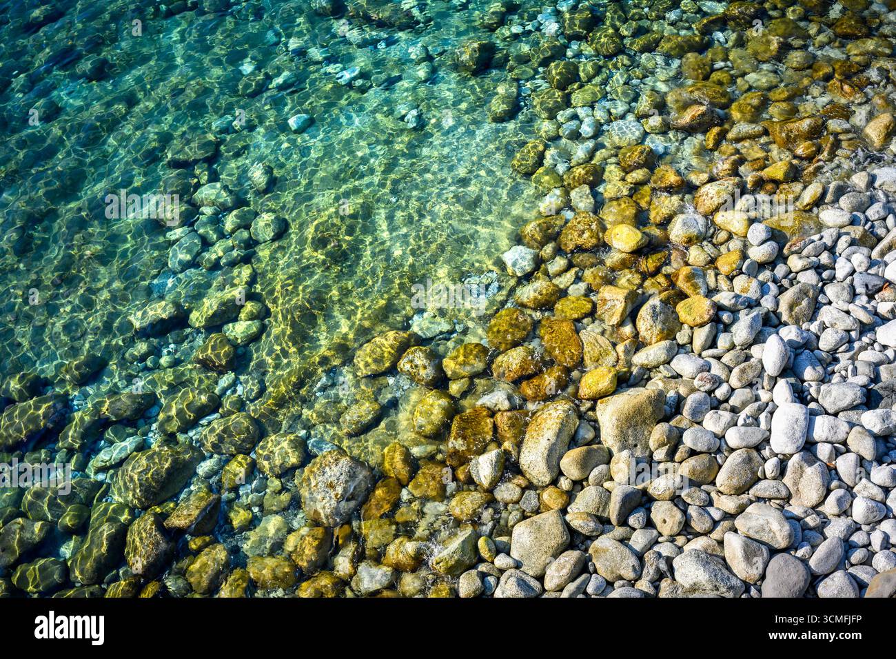 Acque turchesi del Mediterraneo ondulate con pietre rotonde che brillano alla luce del sole. Concetto di vacanza estiva Foto Stock