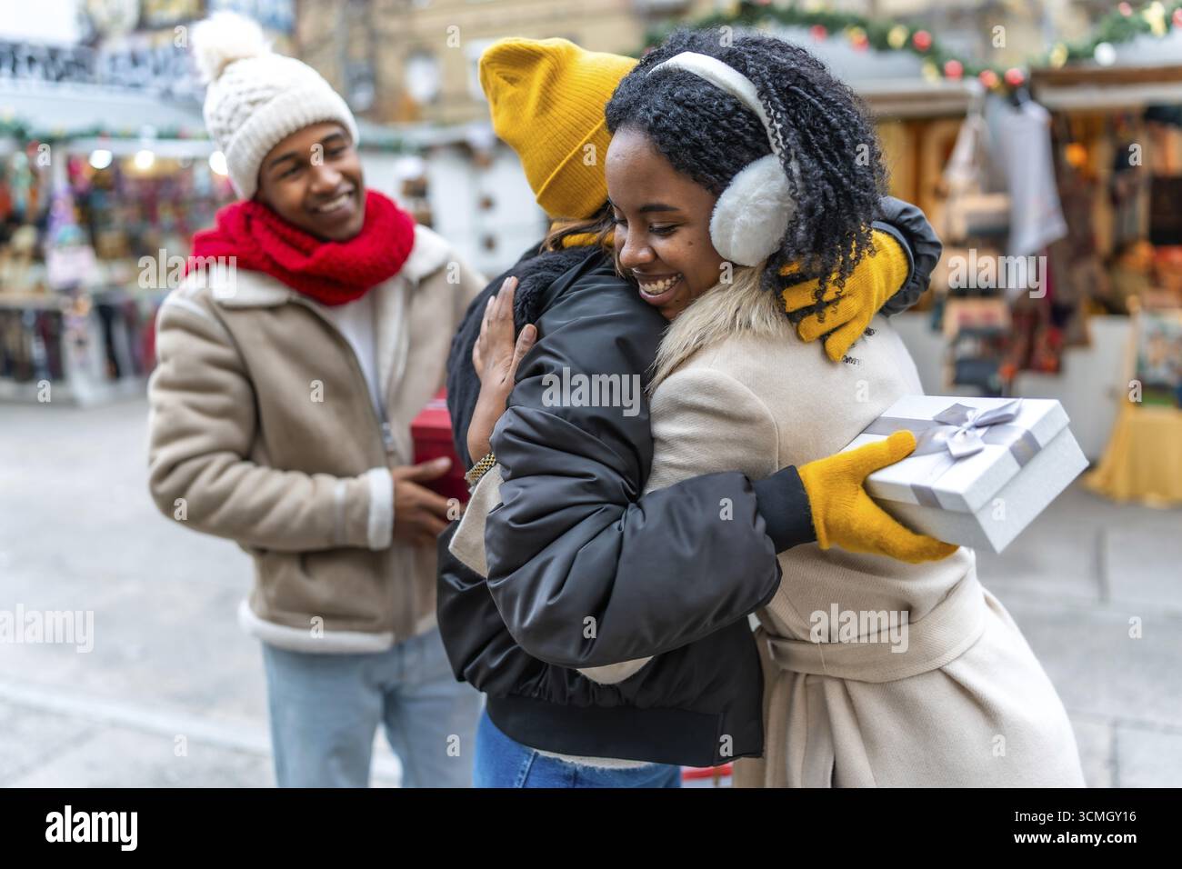 Amici felici che si scambiano regali di natale e si abbracciano al mercatino di natale durante le vacanze invernali Foto Stock