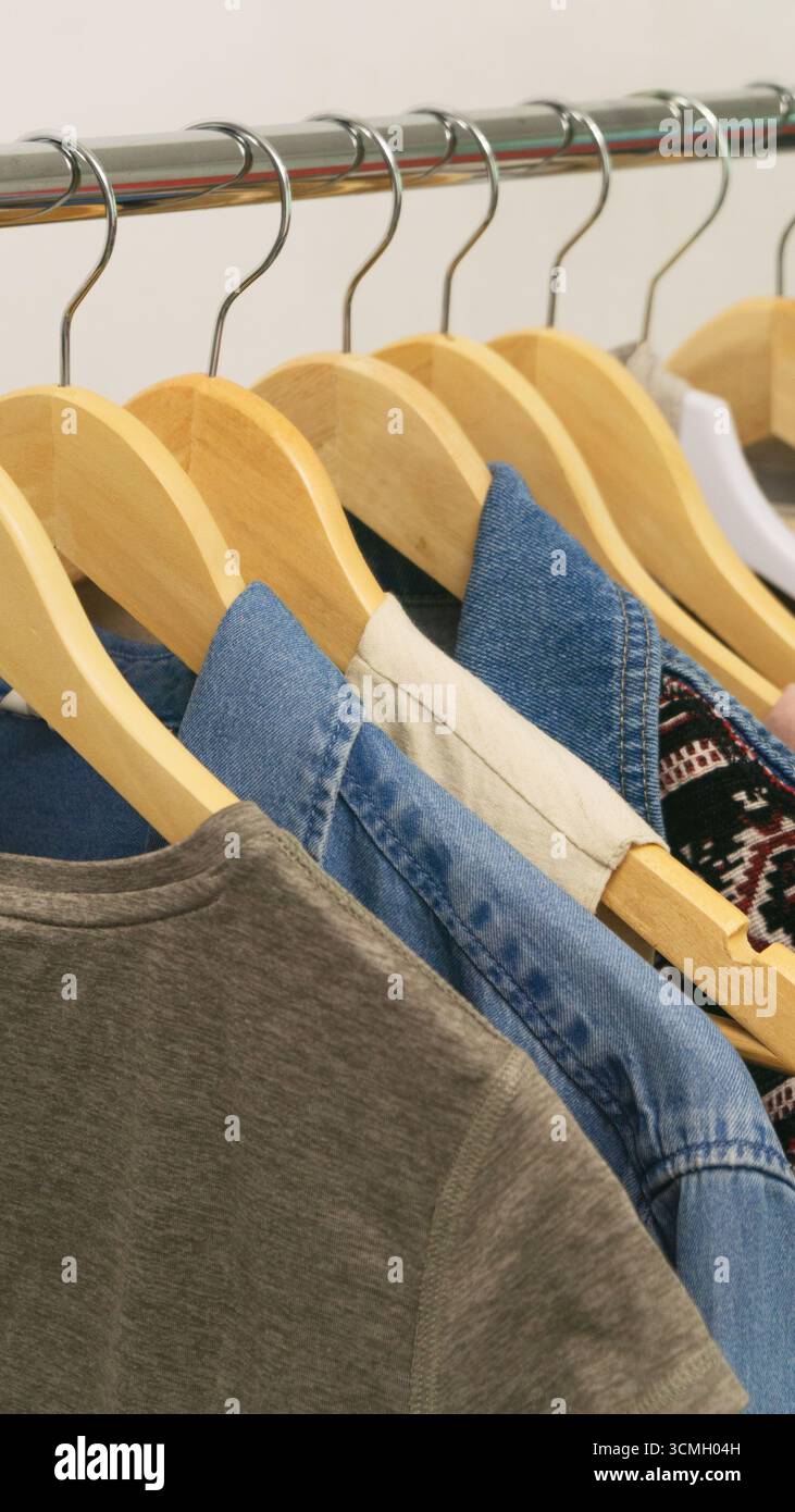 Una collezione di camicie in denim di seconda mano è ordinata su appendiabiti in legno. Questa esposizione di moda aggiornata mette in risalto l'abbigliamento sostenibile. Planet-f Foto Stock