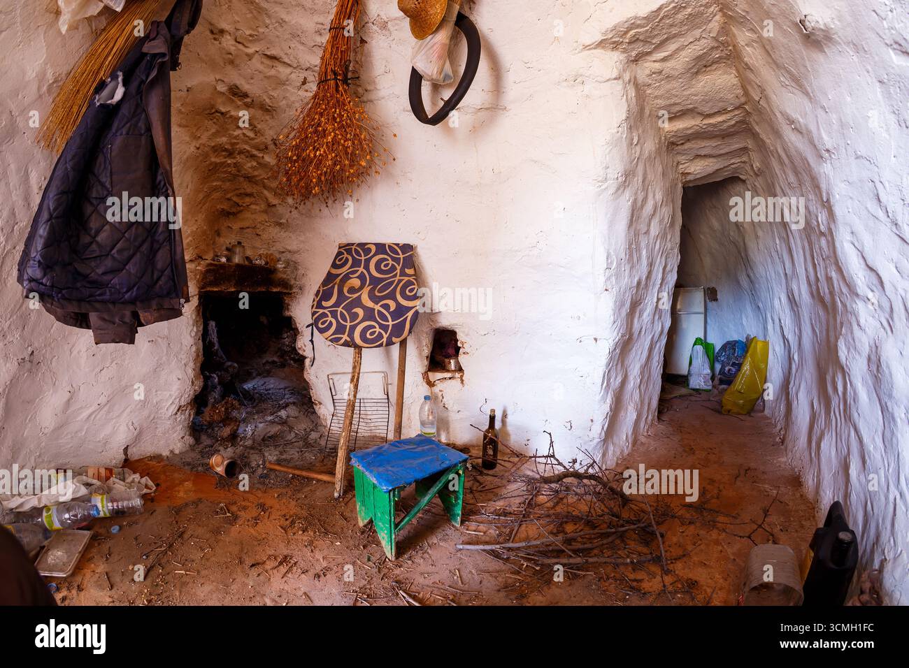 Una vista interna di una camera semplice, simile a una grotta, con pareti ruvide e dipinte di bianco. Vari oggetti, tra cui una sedia, scopa e altri oggetti, sono delle scorribande Foto Stock