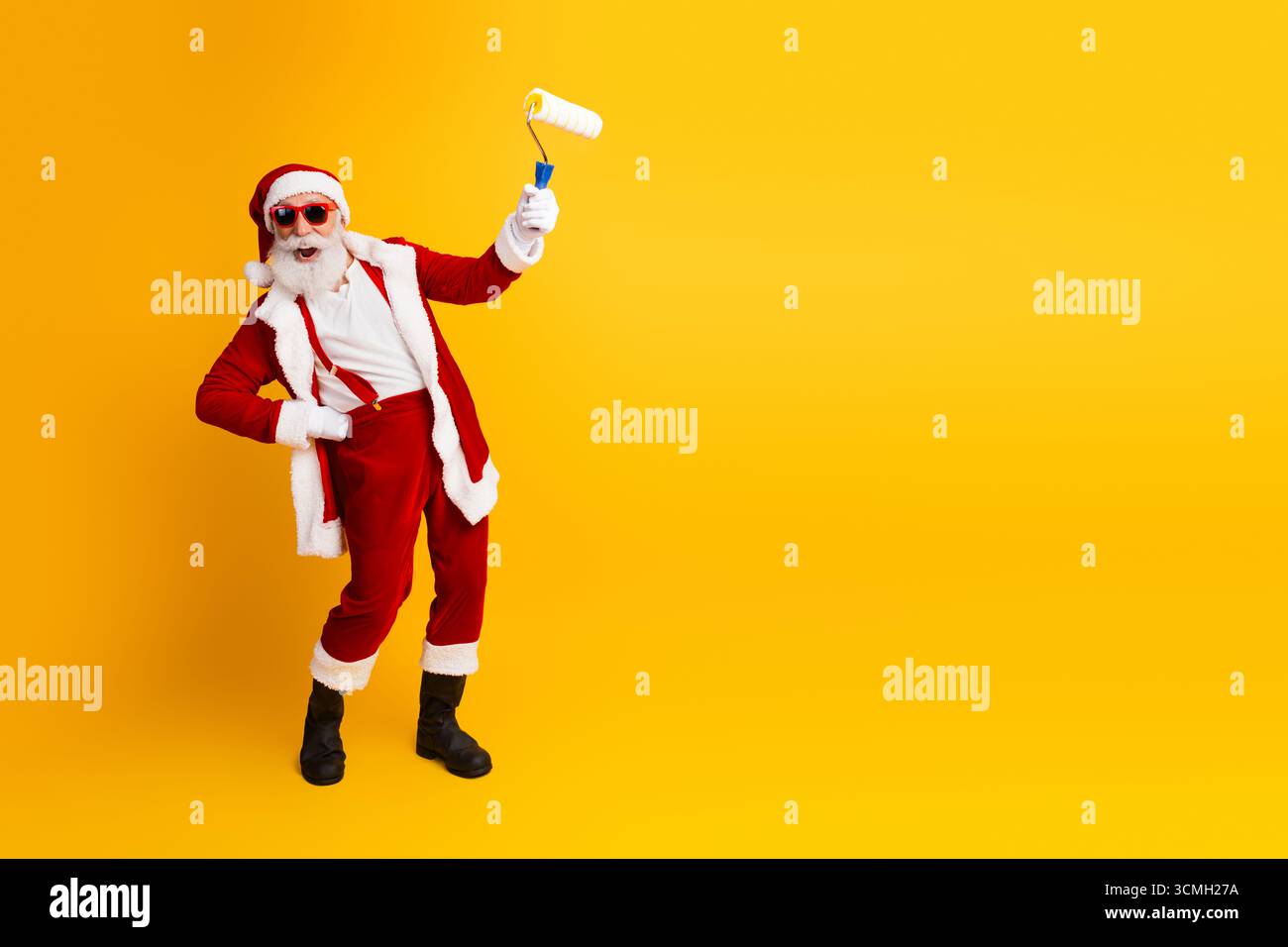 Babbo Natale si diverte in vacanza con un gesto creativo del rullo di pittura su un vibrante sfondo giallo in spirito festoso Foto Stock
