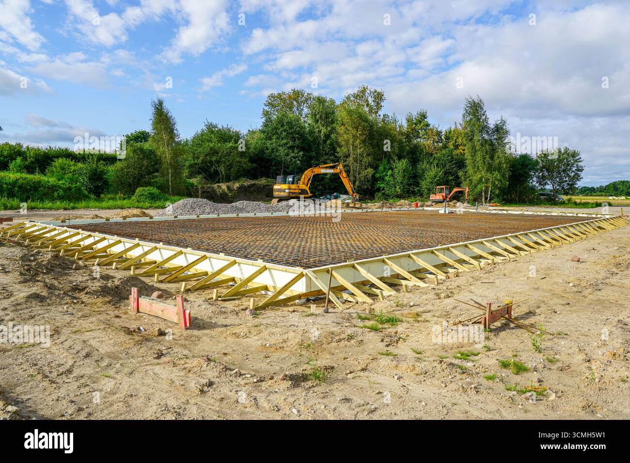 Fondamenta per edifici preparate con griglia in armatura in acciaio e cassaforma in legno, pronte per il versamento di solette in calcestruzzo nel cantiere con escavatori Foto Stock