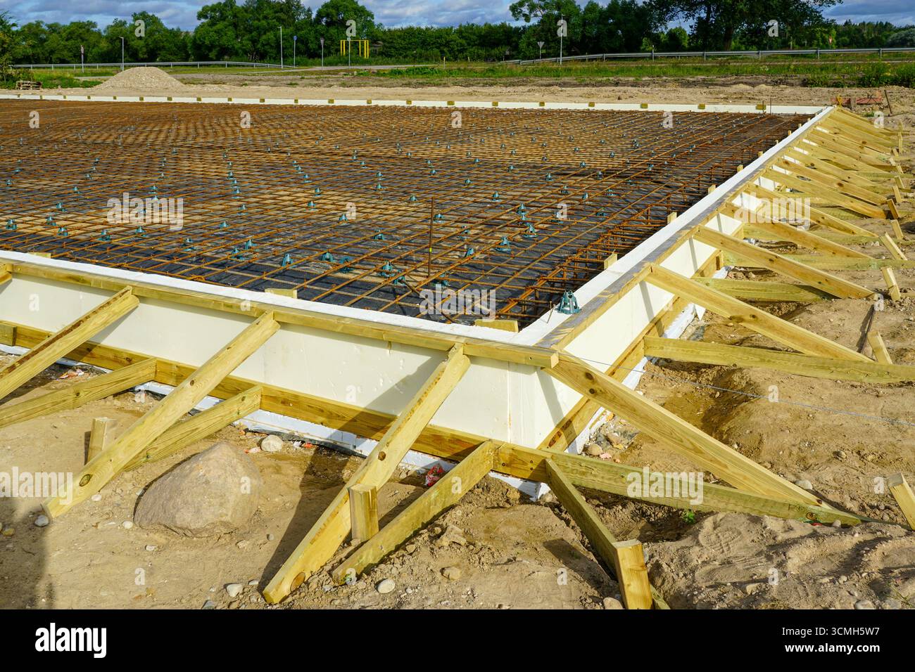 Primo piano di fondamenta termoisolate con griglia di armatura in acciaio rinforzato e cassaforma in legno preparata per il versamento di solette in calcestruzzo in un cantiere Foto Stock