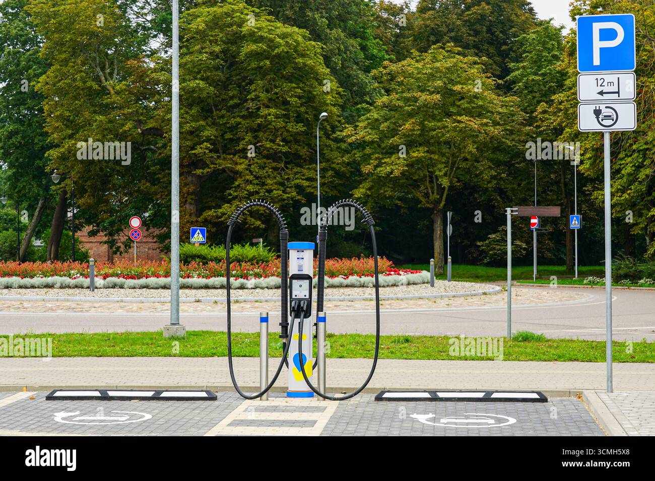 Stazione di ricarica pubblica per auto elettriche con due cavi di ricarica, posti auto EV contrassegnati e segnali stradali in un ambiente urbano Foto Stock