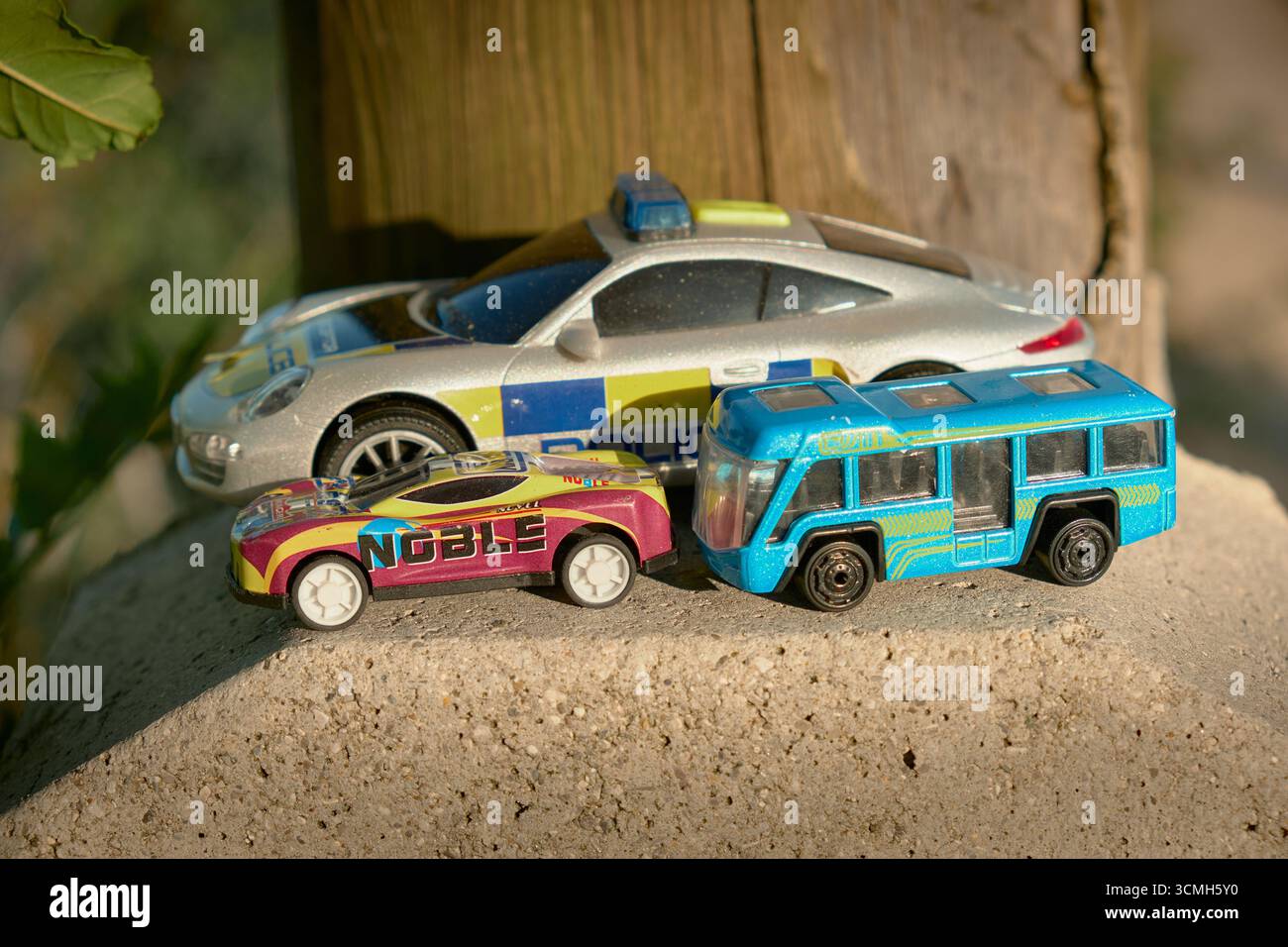 Foto orizzontale di piccole auto giocattolo disposte su un piedistallo di legno. Dietro di loro, un palo in legno rustico aggiunge consistenza, creando un'atmosfera intima e giocosa Foto Stock