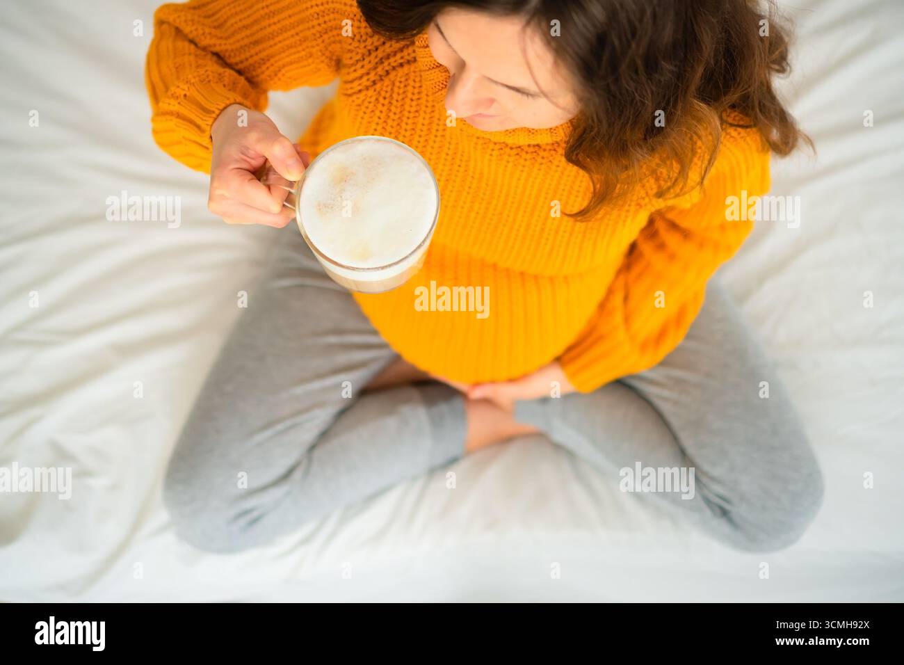 Primo piano aereo di donne incinte che si godono il latte in posa meditativa, riflettendo sulle linee guida alimentari. Calda atmosfera di piacere consapevole. Foto Stock