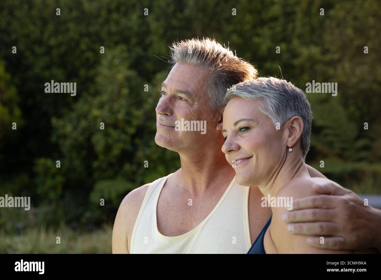 Coppia senior in piedi insieme nel giardino sul retro sotto la luce del sole del pomeriggio Foto Stock