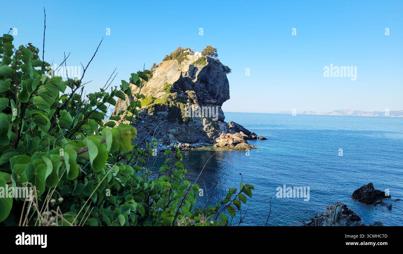 Un piccolo isolotto roccioso con vegetazione verde nelle calme e limpide acque turchesi del Mar Mediterraneo in una giornata di sole Foto Stock
