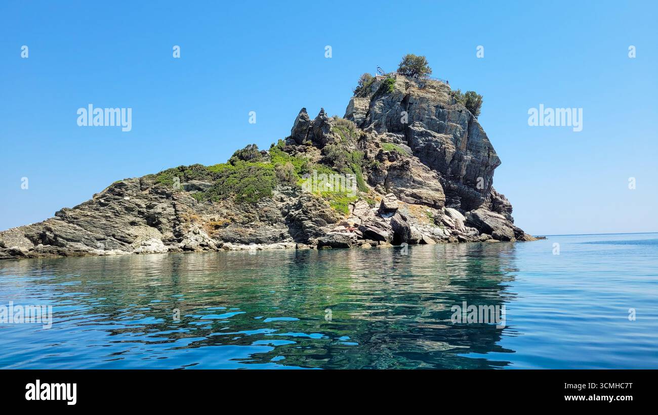 Un piccolo isolotto roccioso con vegetazione verde nelle calme e limpide acque turchesi del Mar Mediterraneo in una giornata di sole Foto Stock