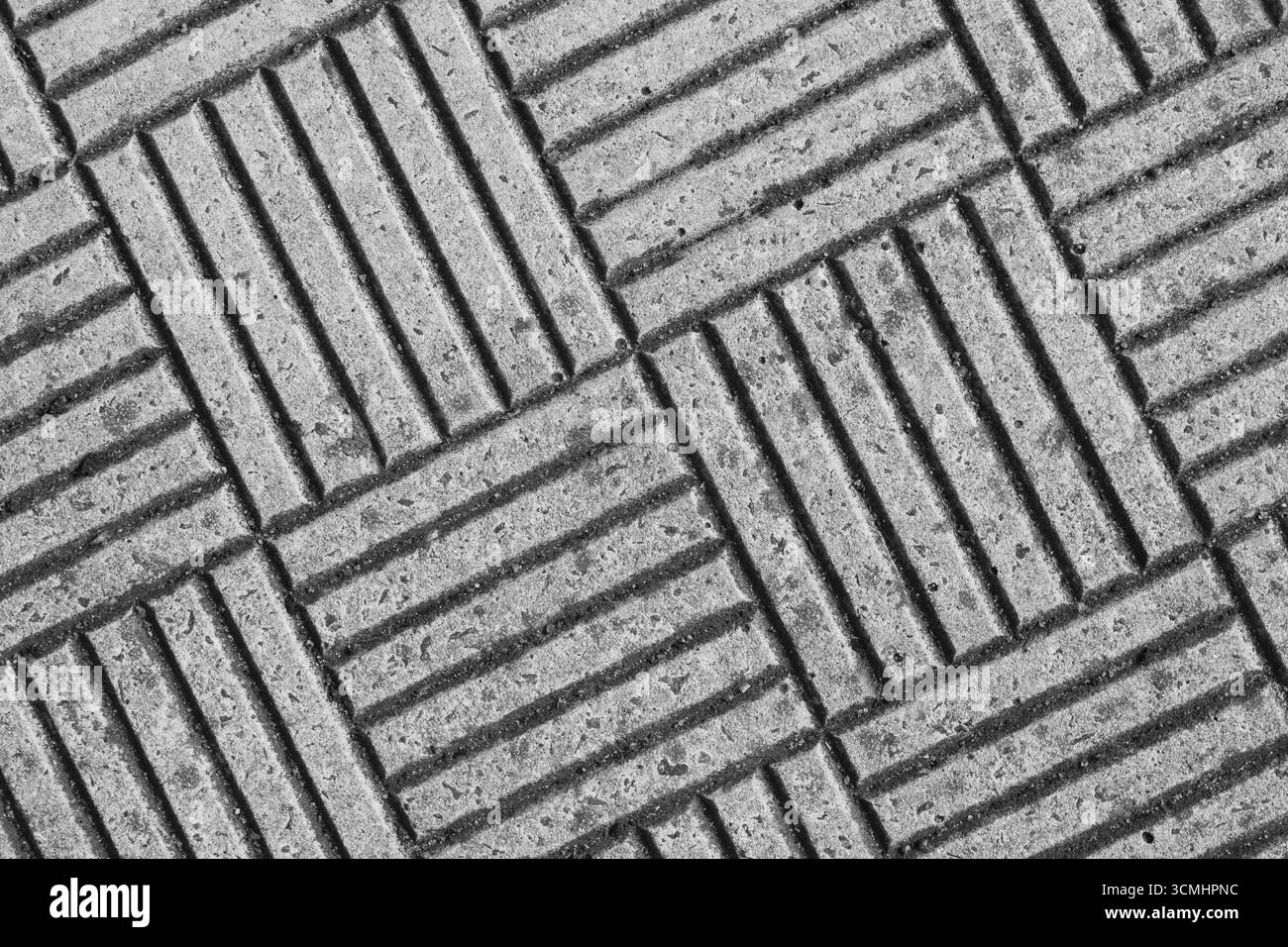La superficie presenta una vista ravvicinata del calcestruzzo testurizzato che presenta scanalature diagonali e un motivo unico. Le tonalità monocromatiche sottolineano il design Foto Stock