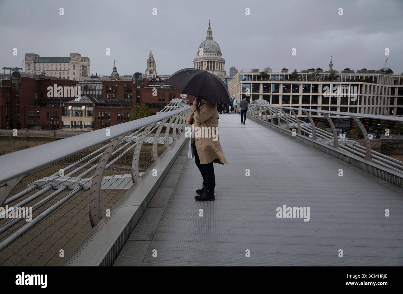 Un cittadino che tiene in mano un ombrello in un pomeriggio ventoso attraverso il Millennium Bridge verso la City di Londra, Inghilterra, Regno Unito Foto Stock