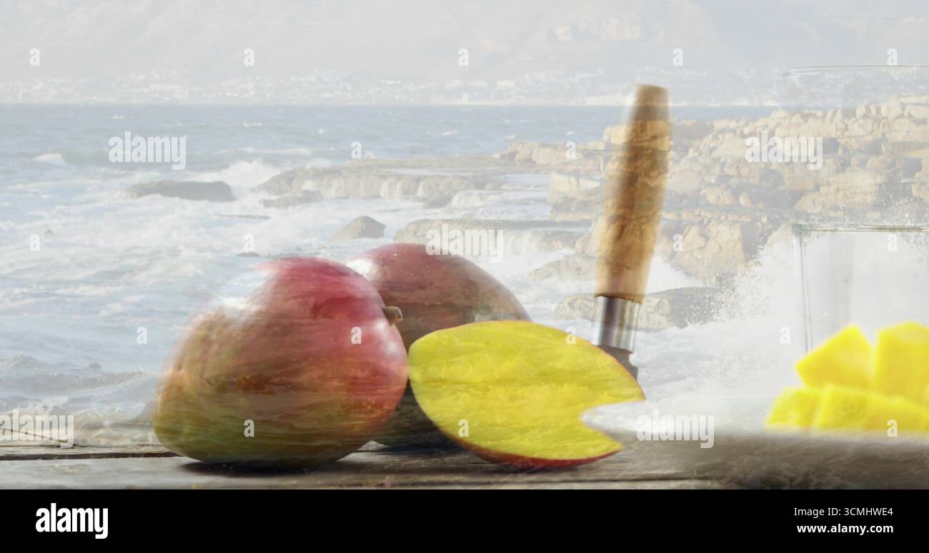 Gruppo di manghi seduti su un tavolo di legno, con coltello da cucina, piatto di cubetti e vetro Foto Stock