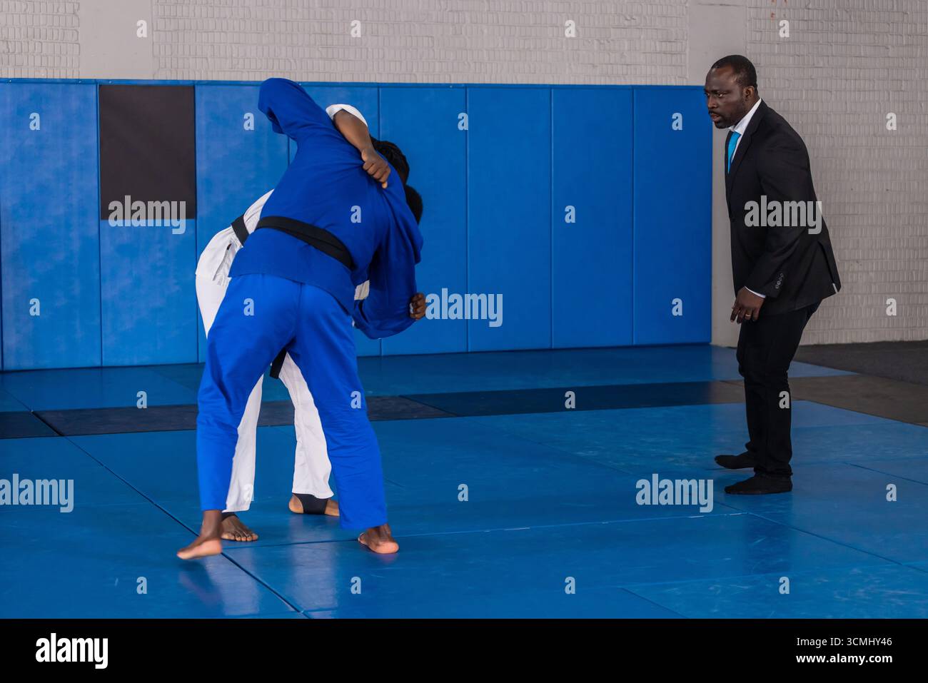 Istruttore afroamericano che supervisiona diversi studenti maschi che si scontrano sui tappetini nel dojo in gis Foto Stock