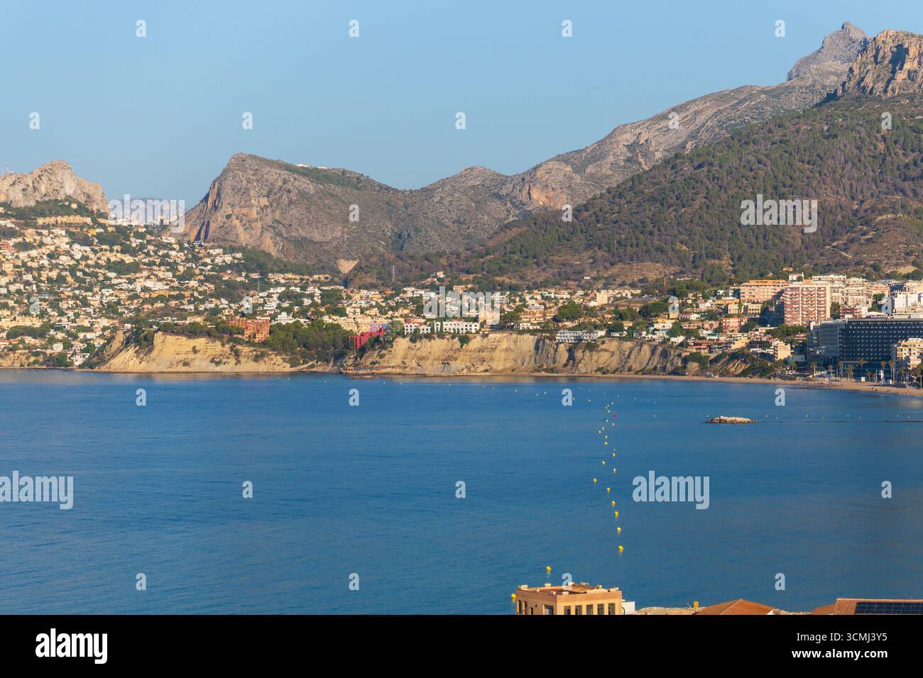 Vista pittoresca della baia di Calpe al mattino. La falesia ha un mare blu calmo con boa gialla che conduce verso le montagne sullo sfondo. Foto Stock