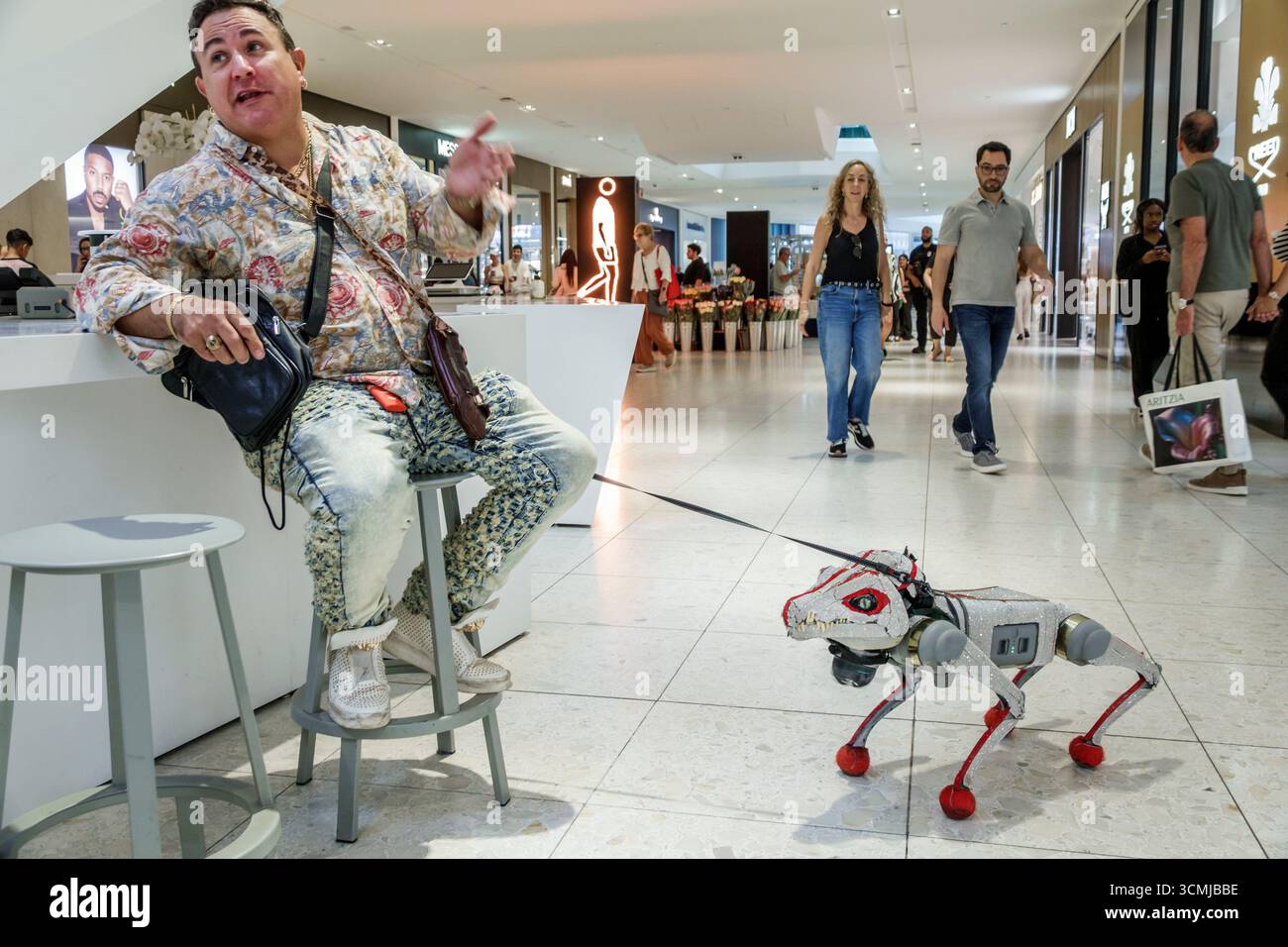 Aventura Mall Miami Florida, negozi interni, uomo seduto su sgabello con guinzaglio robotico, gesti parlanti, posa espressiva, disp. Cani animatronici Foto Stock