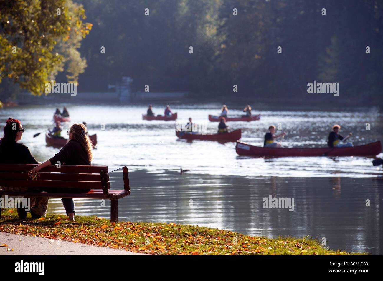 Una tranquilla laguna con canoe e kayak in una mattina nebbiosa, circondata da alberi verdi e una panchina del parco in primo piano. Bowness Park. Calgary Foto Stock