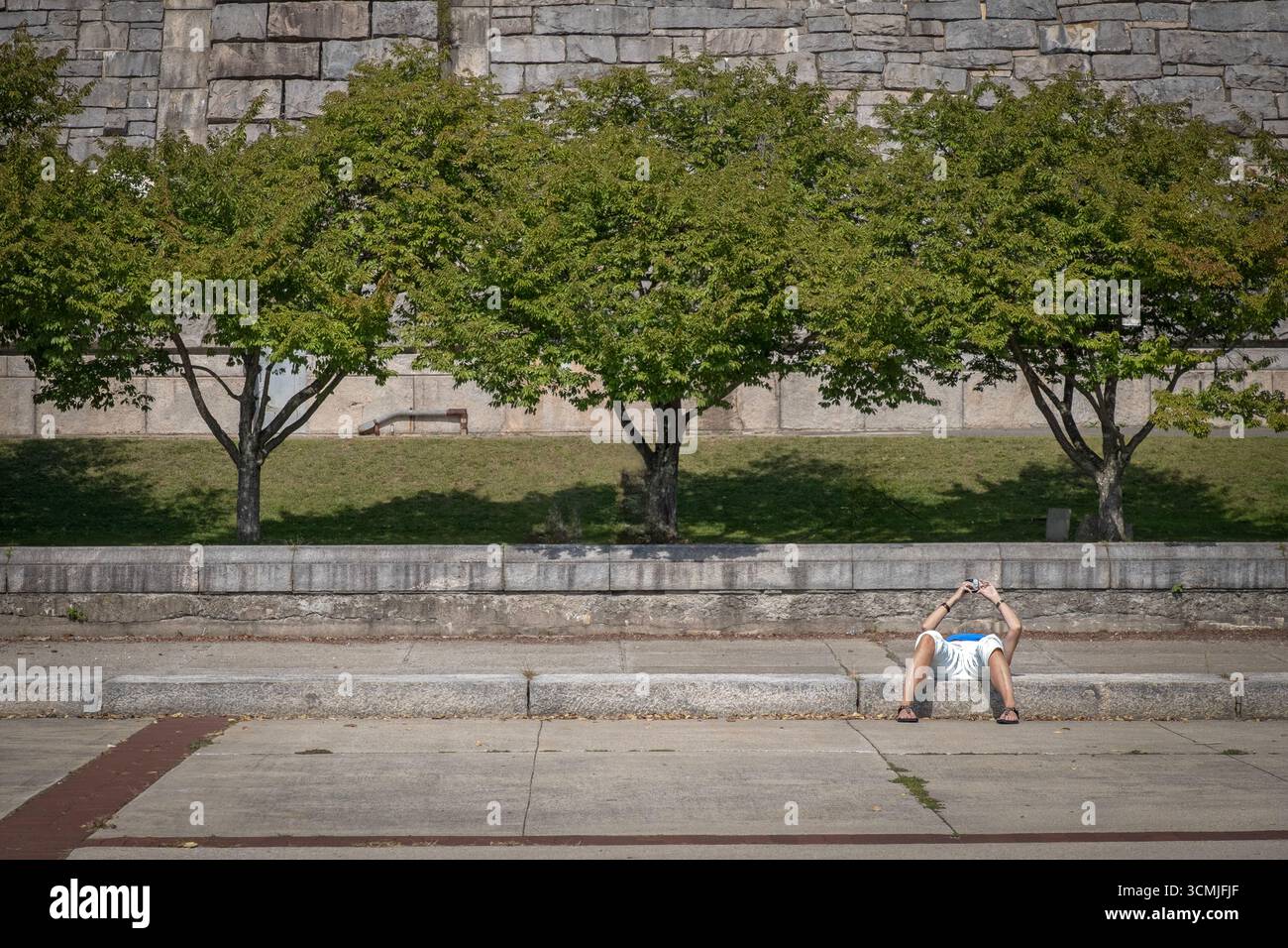 Abbiamo mangiato l'estate al Kensico Dam Plaza. Un uomo legge il suo cellulare mentre è sdraiato all'indietro ed è invisibile. A Valhalla, Westchester, New York Foto Stock