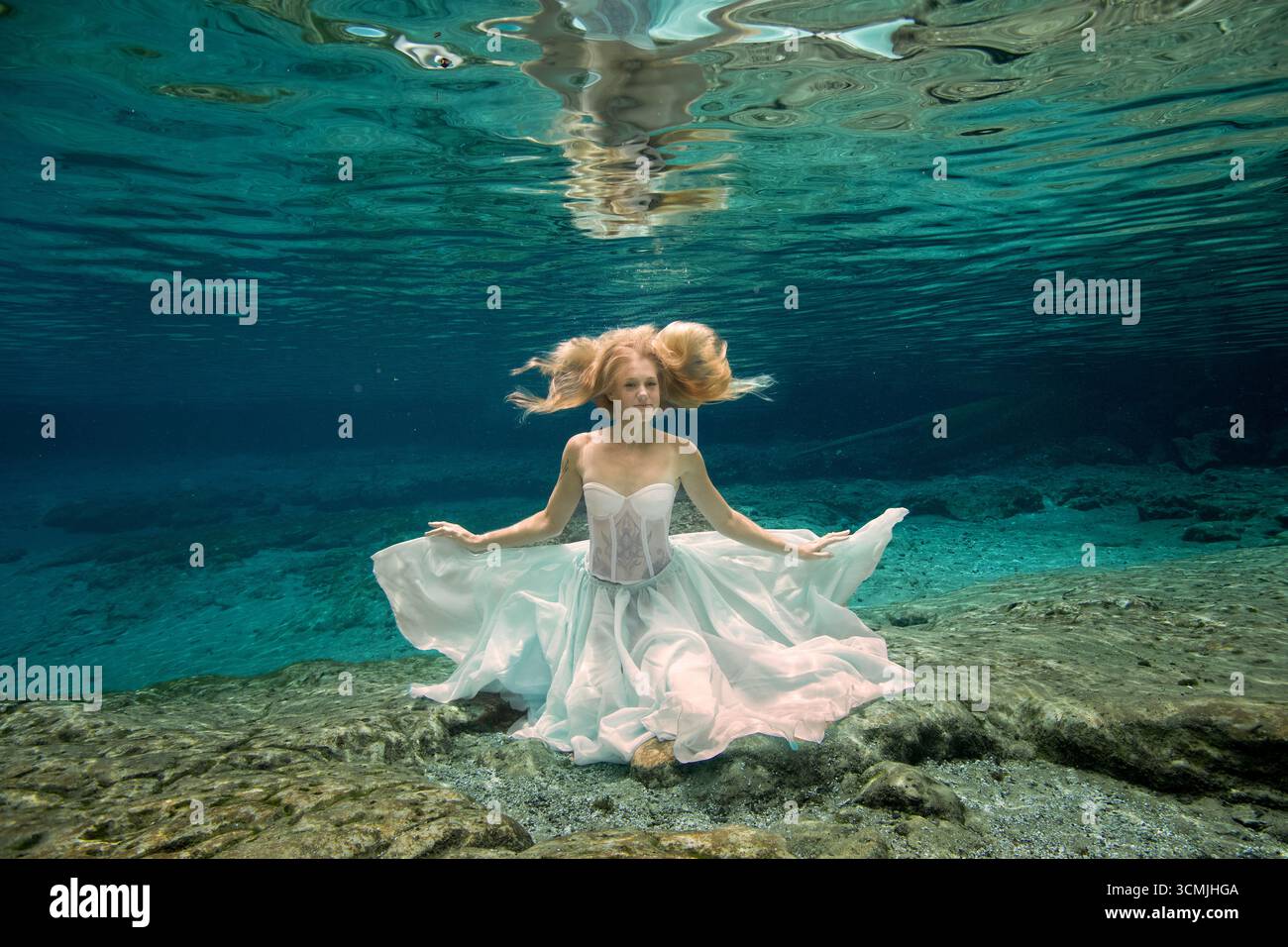 Donna adulta con tatuaggi in un abito senza spalline seduto sott'acqua sul fondo del mare Foto Stock