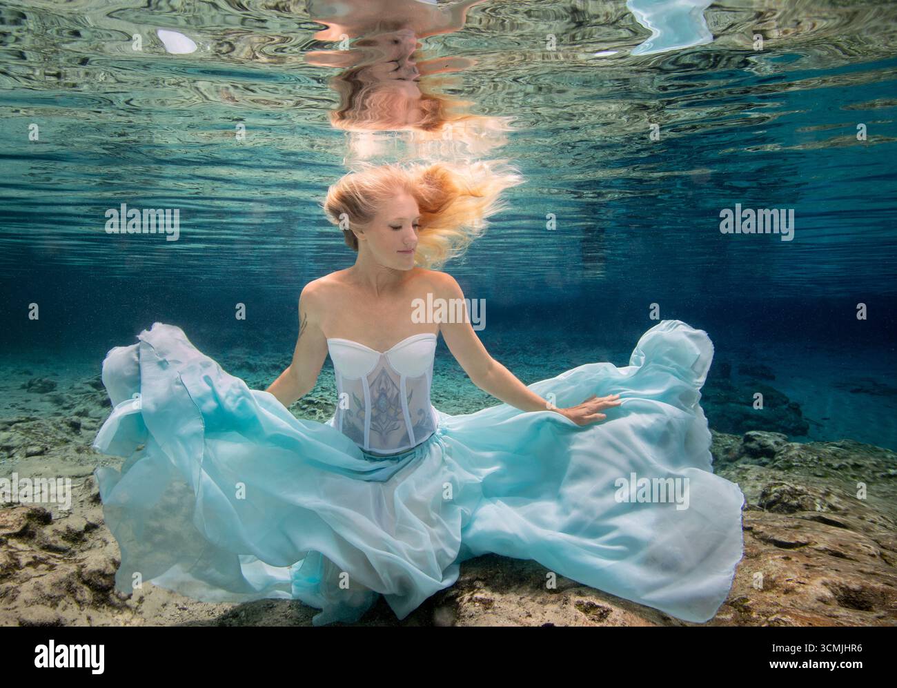 Donna adulta con tatuaggi in un abito senza spalline seduto sott'acqua sul fondo del mare Foto Stock