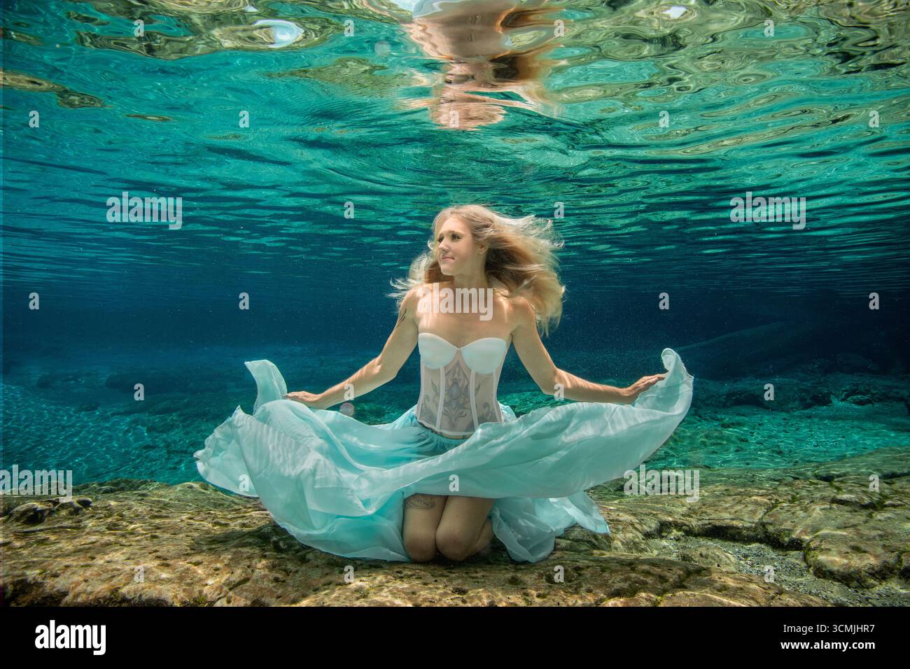 Donna adulta con tatuaggi in un abito senza spalline seduto sott'acqua sul fondo del mare Foto Stock
