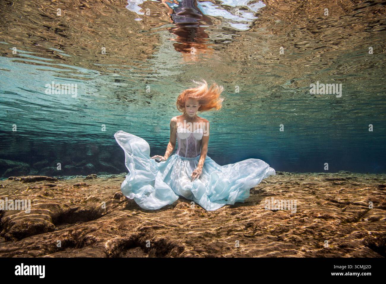 Donna adulta con tatuaggi in un abito senza spalline seduto sott'acqua sul fondo del mare Foto Stock