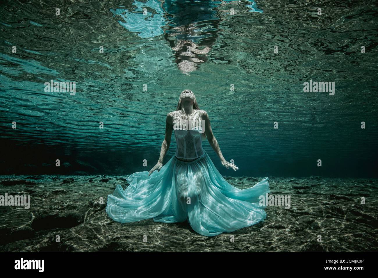 Donna adulta con tatuaggi in un abito senza spalline seduto sott'acqua sul fondo del mare Foto Stock