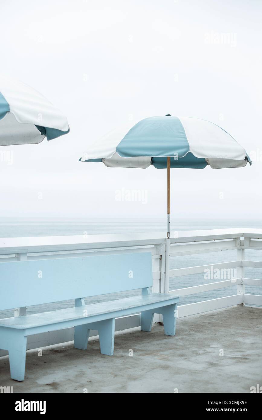 Due ombrelloni a righe e una panca di legno su un molo vicino all'oceano, Malibu, California, USA Foto Stock