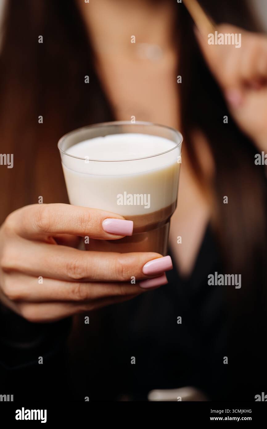 Dessert a strati con crema di latte e cioccolato in un bicchiere, tenuto dalle donne Foto Stock