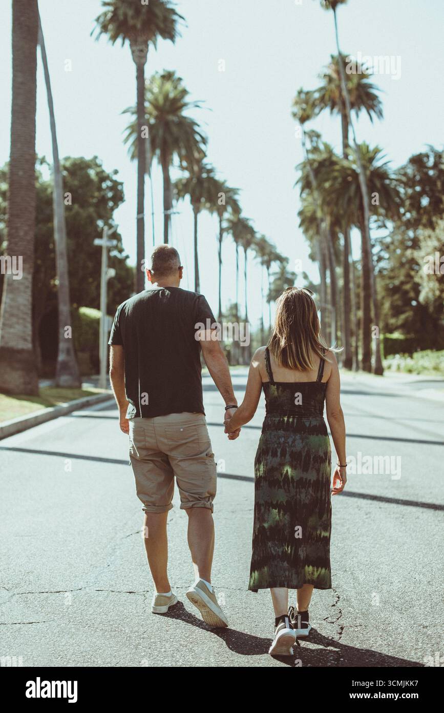 Vista posteriore di una coppia che cammina in mezzo a una strada, Beverly Hills, Los Angeles, California, Stati Uniti Foto Stock