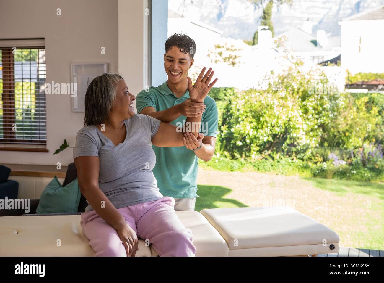 Terapeuta maschile che guida la donna anziana attraverso il braccio allungato su un lettino di trattamento imbottito in camera Foto Stock