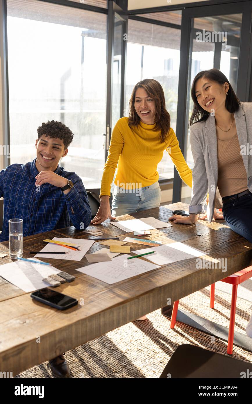 Diversi colleghi di abbigliamento aziendale che si appoggiano al tavolo in ufficio, rivedendo gli schizzi dei progetti Foto Stock