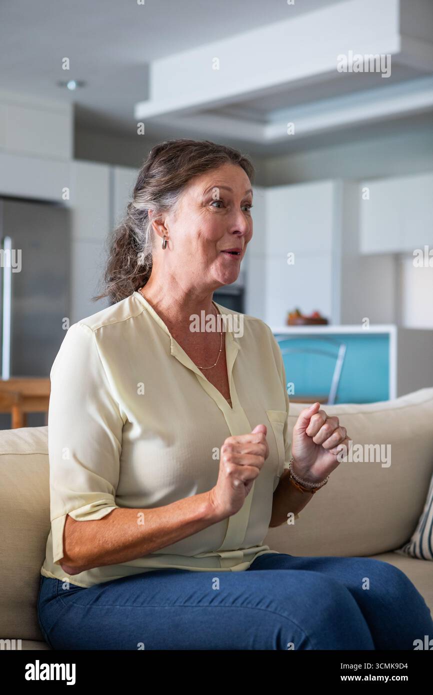 Donna seduta su un divano beige nel soggiorno che parla in modo espressivo con un cestino di frutta nelle vicinanze Foto Stock