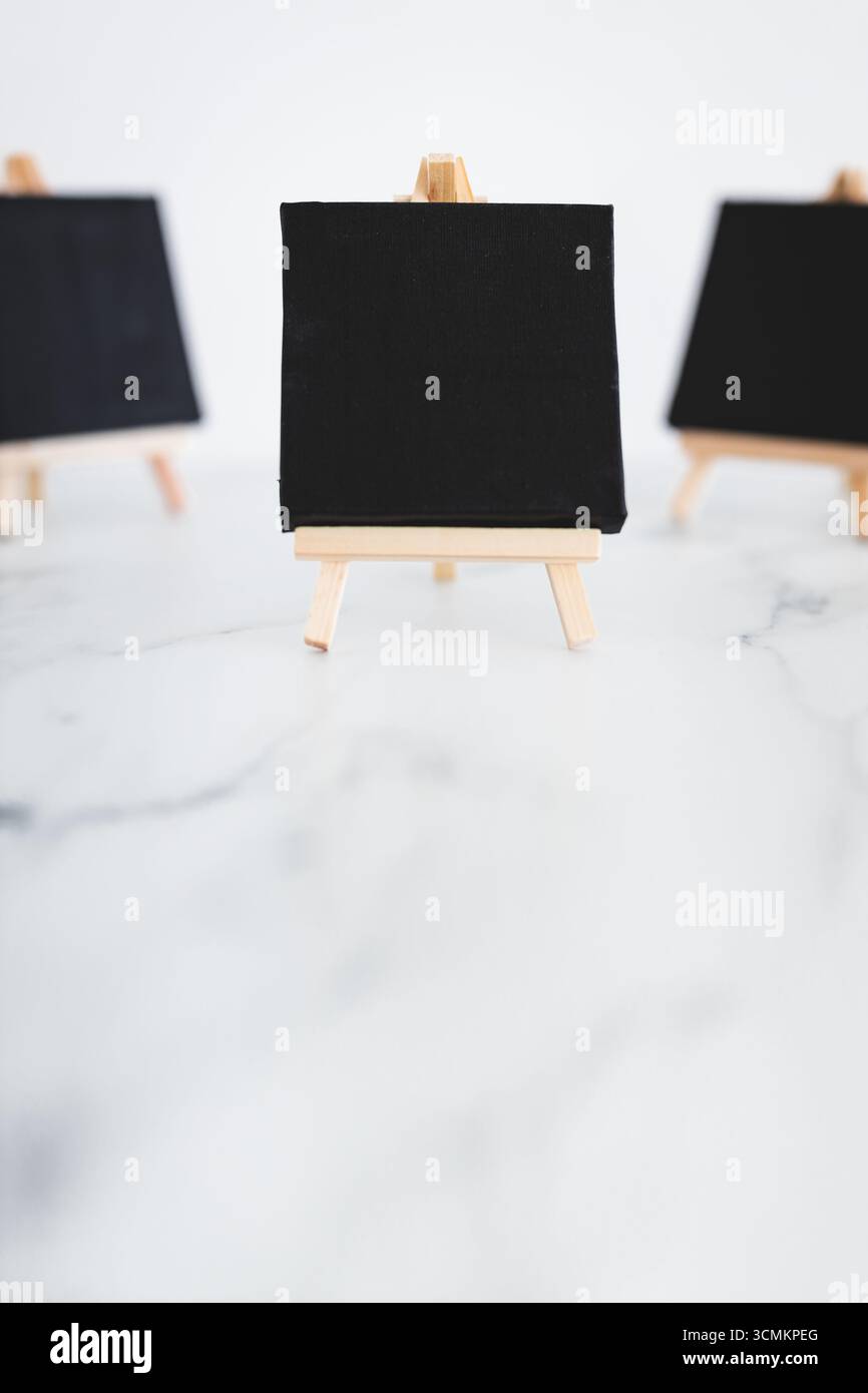 tre tele nere su cavalletti miniaturizzati su scrivania in marmo bianco, sfondo mockup minimalista per aggiungere testo o design, dof poco profondo Foto Stock tre tele nere su cavalletti miniaturizzati su scrivania in marmo bianco, sfondo mockup minimalista per aggiungere testo o design, dof poco profondo Foto Stock