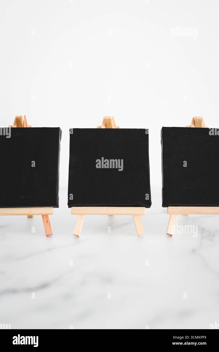 tre tele nere su cavalletti miniaturizzati su scrivania in marmo bianco, sfondo mockup minimalista per aggiungere testo o design, dof poco profondo Foto Stock tre tele nere su cavalletti miniaturizzati su scrivania in marmo bianco, sfondo mockup minimalista per aggiungere testo o design, dof poco profondo Foto Stock