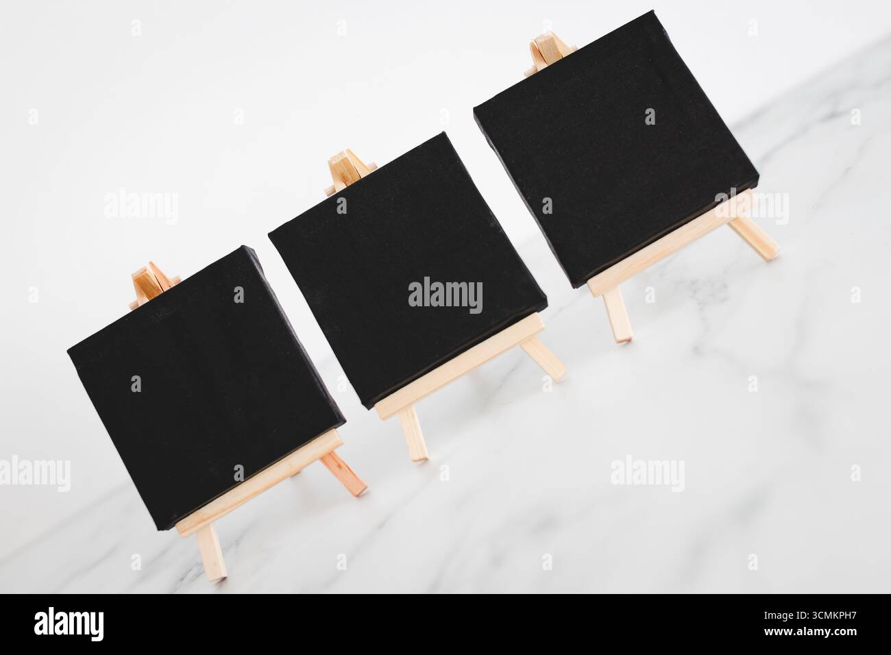 tre tele nere su cavalletti miniaturizzati su scrivania in marmo bianco, sfondo mockup minimalista per aggiungere testo o design, dof poco profondo Foto Stock tre tele nere su cavalletti miniaturizzati su scrivania in marmo bianco, sfondo mockup minimalista per aggiungere testo o design, dof poco profondo Foto Stock