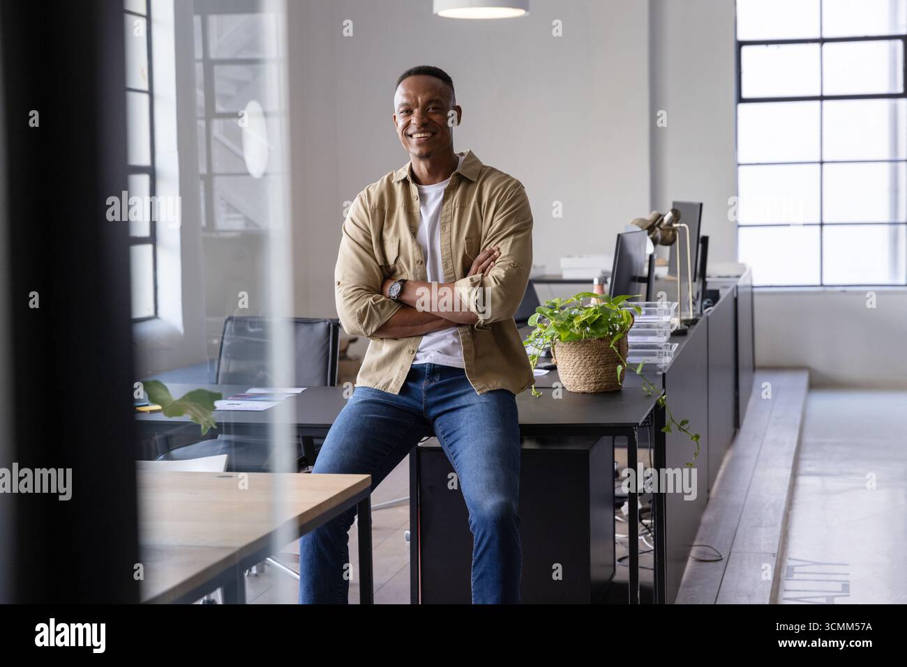 Uomo afro-americano seduto sulla scrivania in ufficio con monitor sorridendo alla fotocamera Foto Stock